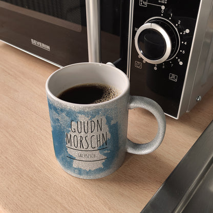 Hallo auf Sächsisch Guudn Morschen lustiger Glitzer-Kaffeebecher mit blauem Hintergrund