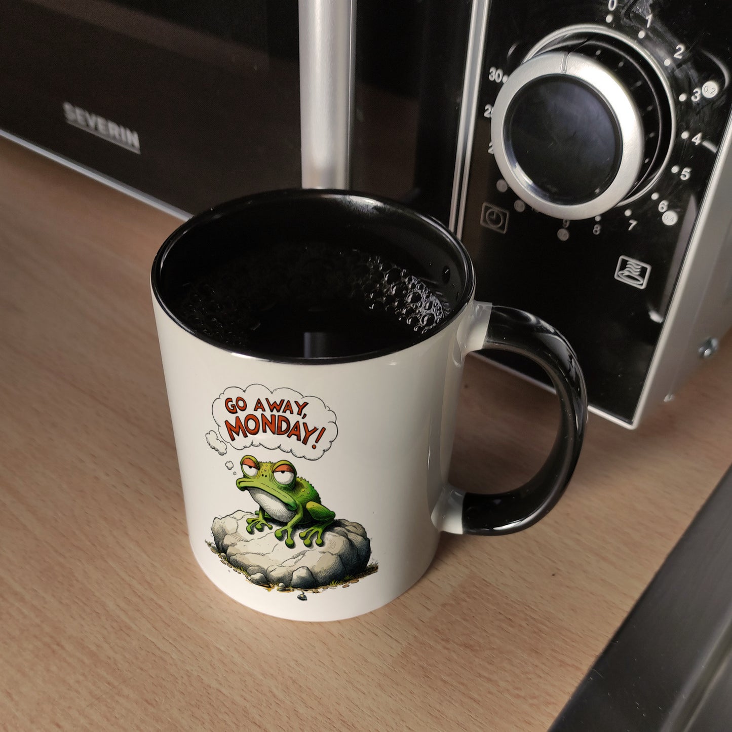 Mürrischer Frosch auf Stein Kaffeebecher in schwarz mit Spruch Go away, Monday!