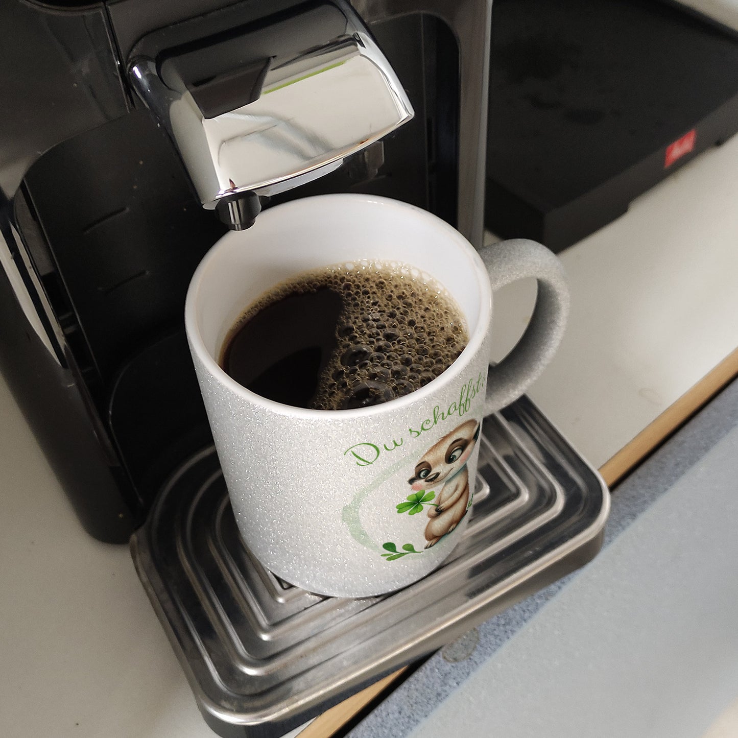 Erdmännchen mit Kleeblatt Glitzer-Kaffeebecher mit Spruch Du schaffst das